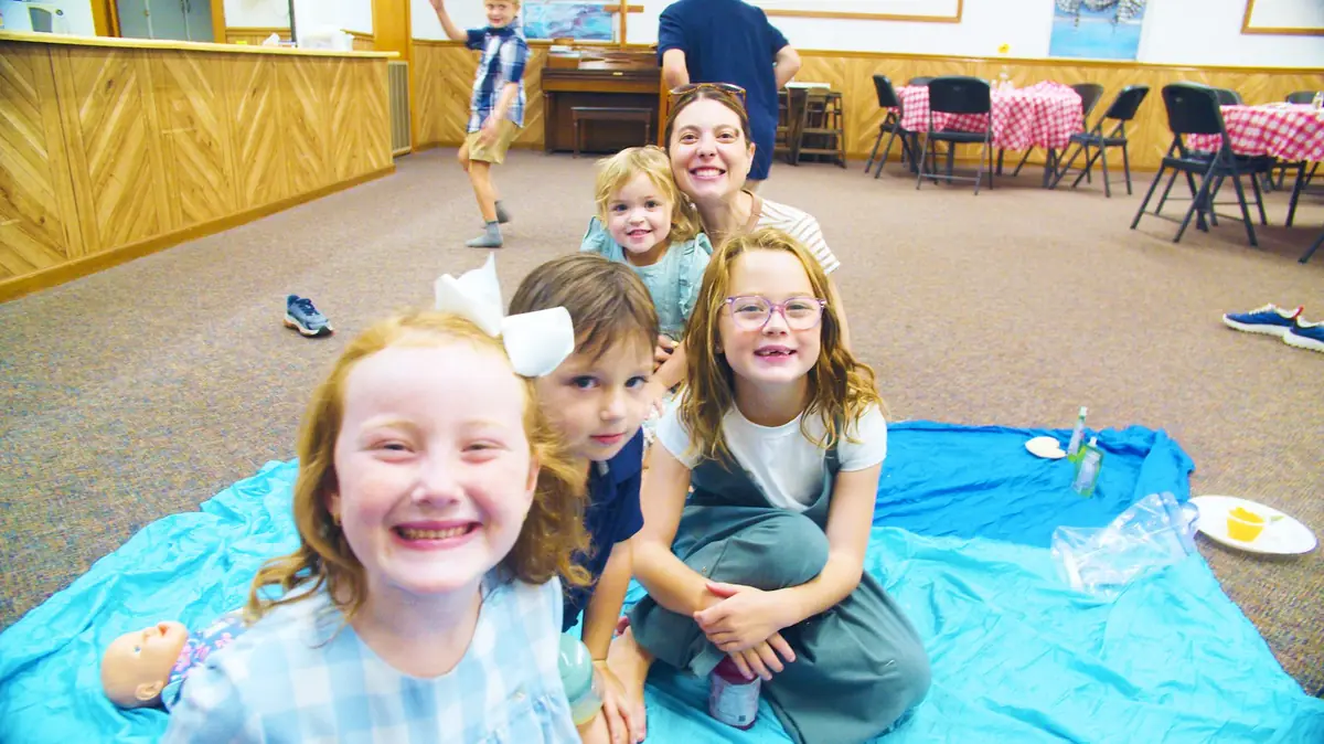 Smiling girls and a mom sitting on a picnic blanket in the fellowship hall